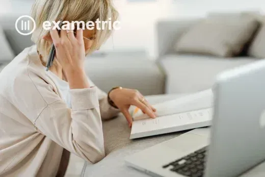 Coordenadora pedagógica analisando dados educacionais em laptop com livro e caneta ao lado, luz natural